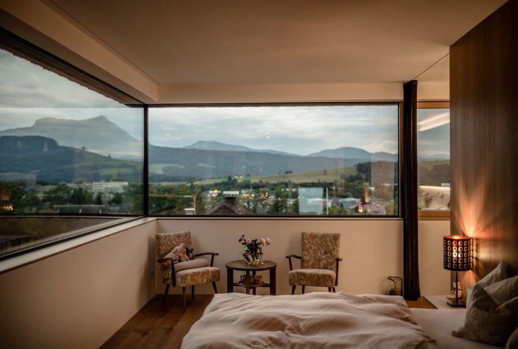 Ein modernes Schlafzimmer mit großen Fenstern, die einen Blick auf malerische Berge und Landschaften bieten, sowie stilvolle Möbel und eine gemütliche Atmosphäre.