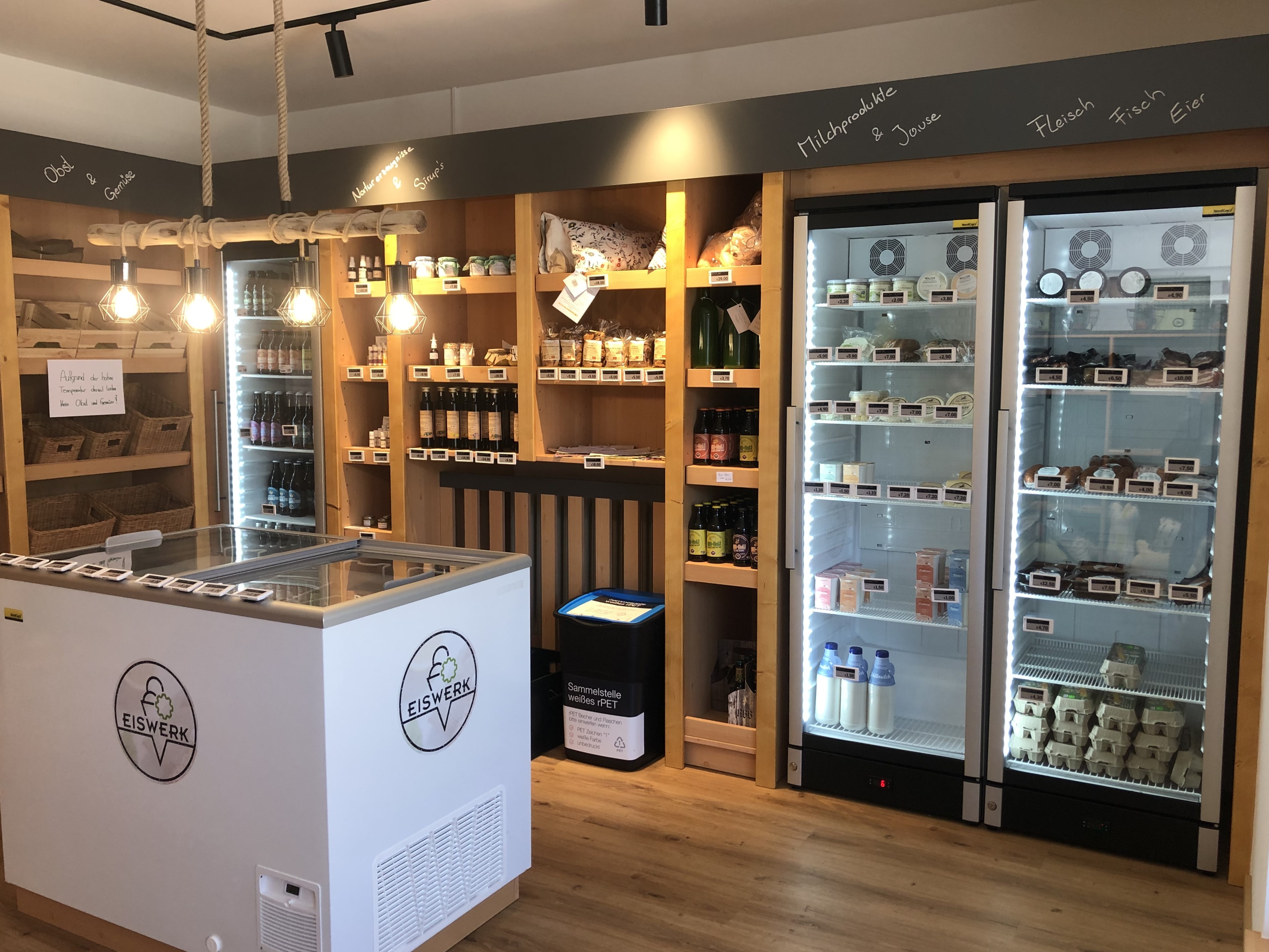 Ein Blick in ein modernes Geschäft mit Warenregalen und Kühlschränken, die verschiedene Produkte wie Milch, Fleisch und Getränke anbieten.